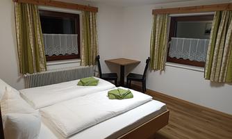 A cozy bedroom with two beds and fresh towels. The room has wooden flooring and bright curtains.
