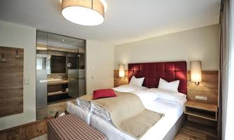 A modern bedroom with a large bed and a red headboard. There are wooden and glass elements, as well as soft lighting.