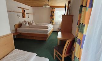 A cozy hotel room with two beds and a desk. Large windows provide plenty of daylight.