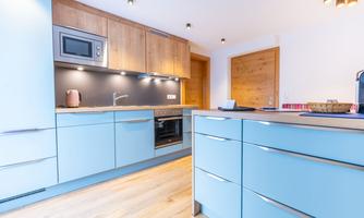A modern kitchen with light blue cabinets and wooden details. It is well lit and tidy.