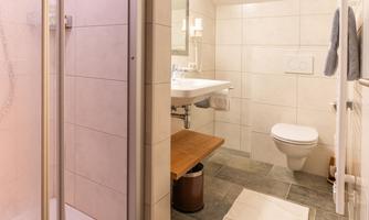 A modern bathroom with a shower, a sink, and a toilet. The floor is tiled with gray tiles and there is a small rug.