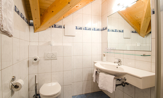 A modern bathroom with white tiles and wooden details. It features a sink, a toilet, and a large mirror.