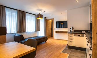 A modern living room with a cozy couch and a dining area. The kitchen is well-equipped and the room has large windows with curtains.
