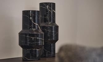 Two elegant vases made of black marble with golden veining are placed on a shelf. The contemporary shape adds a modern touch to the room.