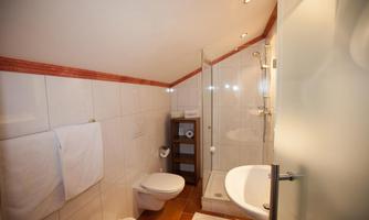 A modern bathroom with a shower and a toilet. The walls are tiled and there are fresh towels.