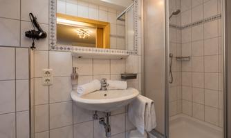 A modern bathroom with a shower and a sink. There are towels and a large mirror.