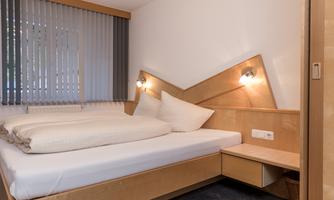 A modern bedroom with a double bed and soft lighting. The walls are in light wood and gray tones.