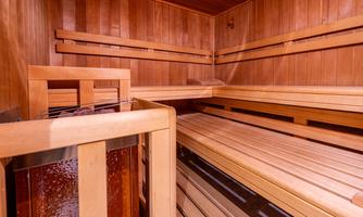 A bright sauna with wooden paneling and several wooden loungers. The room radiates warmth and relaxation.