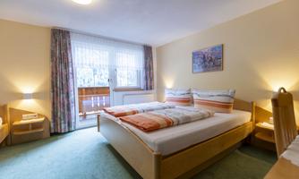 A cozy bedroom with two beds and colorful cushions. Large windows bring in plenty of daylight.