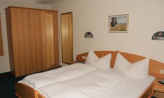 A cozy bedroom with a large bed and two pillows. A wardrobe and a mirror are also present in the room.