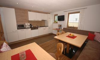 A modern kitchen with wooden details and a cozy dining area. The table is decorated with a red tablecloth and fresh fruits.