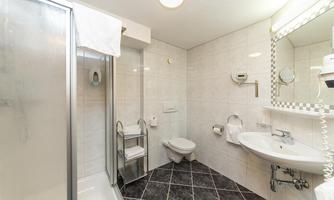 A modern bathroom with a shower, sink, and toilet. The walls are brightly tiled and the floor has an elegant pattern.