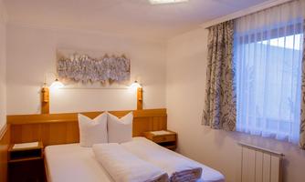 A cozy bedroom with a double bed and two pillows. The walls are light, and a window lets in natural light.