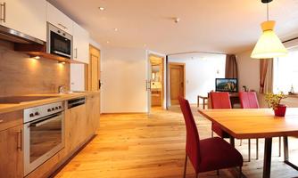 A modern kitchen with wooden shelves and appliances. The dining area has a wooden table and red chairs.