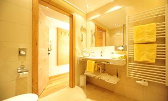 A modern bathroom with bright walls and wood details. Yellow towels are laid out on the sink and a shower is visible.