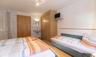 A simple room with two single beds and a sofa bed. There is a wardrobe, a sink, and a shower area.