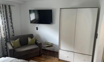 A modern bedroom with a cozy sofa and a large wardrobe. A television is mounted on the wall, and the floor is made of wood.