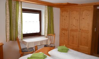A cozy room with two bed frames and a wooden wardrobe. 

By the window are green curtains and a small table with chairs.