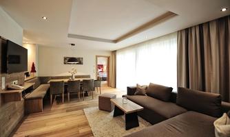 A modern living room with a cozy sofa and a wooden table. The room is bright and has a dining area with elegant chairs.