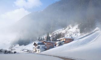 A snowy landscape with modern houses on the hillside. The sky is overcast and there is fog over the mountains.