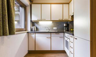 A modern kitchen with white cabinets and wood details. It features a kettle and a coffee machine as well as a stove and an oven.