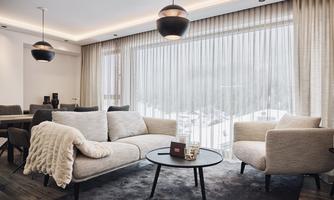 A modern apartment with a cozy living room. Large windows with curtains offer a view of the winter landscape outside.