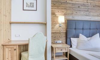 A cozy bedroom with a wooden desk and a padded bed. The walls are in warm wood tones, creating an inviting atmosphere.