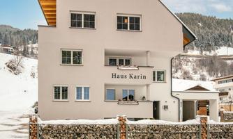 A modern building named "Haus Karin" in a snow-covered environment. The facade is friendly and inviting, surrounded by a rock garden.