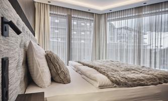 A modern bedroom with a cozy bed and elegant curtains. Large windows let in plenty of light and provide a view outside.