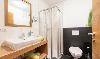 A modern bathroom with a shower, a sink, and a toilet. It is bright and friendly designed, featuring wood and white elements.