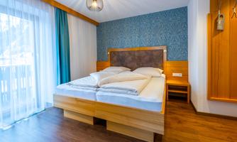 A cozy bedroom with a large bed and minimalist decor. Large windows provide plenty of daylight and a pleasant atmosphere.