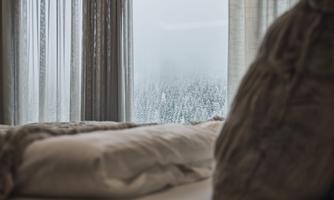 A cozy bedroom with a view of snow-covered trees. The curtains let in soft light.