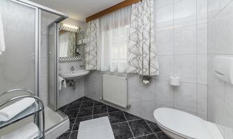 A modern bathroom with a glass shower and a sink. The walls are clad with light tiles and there are towels on a shelf.