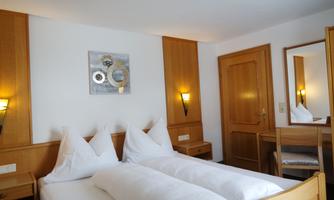 A cozy room with two beds and light wood details. A decorative picture hangs on the wall and a mirror stands on the desk.