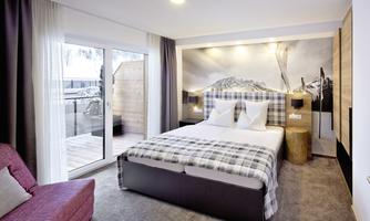 A modern bedroom with a large bed and a view of the mountains. The room is bright and inviting, with a cozy armchair and a large window.