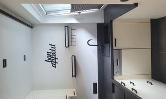 A modern kitchen with black countertops and light cabinets. The inscription "bon appétit" hangs on the wall.