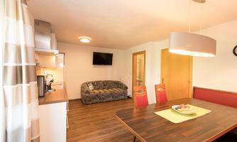 A cozy living kitchen with a dining table, chairs, and a couch. The decor is modern and bright.