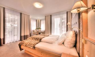 An elegant bedroom with a large bed and soft colors. Large windows let in plenty of daylight and offer a view outside.