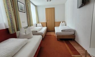 A simple guest room with three single beds and a television. The room is bright and friendly furnished.
