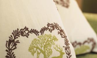 Two cushions with a decorative design of a tree and animals in green and brown. The cushions give the room a rustic and cozy atmosphere.