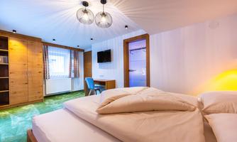 A cozy room with a double bed and modern furnishings. There is a desk, a television, and large windows that make the room bright and inviting.