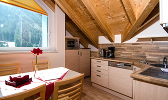 A modern kitchen with wooden elements and a dining area. Large windows offer a view of the mountains.