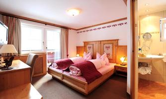 A cozy hotel room with two beds, wood look, and warm colors. The bathroom is modern and right next to the bedroom.
