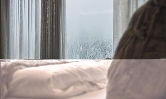A cozy bedroom with a soft bed and gentle curtains. Outside, a foggy landscape can be seen.