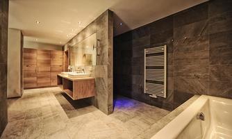 A modern bathroom with an elegant bathtub and wooden furniture. The walls are covered with gray tiles and there is a pleasant lighting.