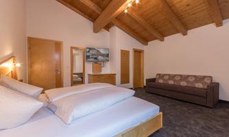A cozy bedroom with a double bed and a sofa. The wooden ceiling and warm colors give the room an inviting atmosphere.
