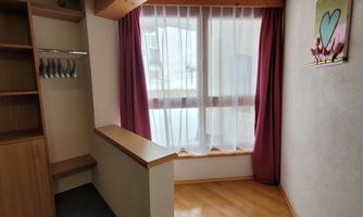 A bright room with a large window and a cozy seating area. The walls are plain, with a small picture on the wall.