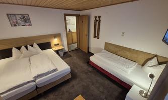 A cozy hotel room with two beds and a table. The room has wooden walls and a television.