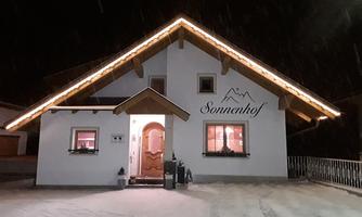 A cozy house in the snow, festively illuminated. The sign reads "Sonnenhof".