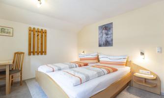 A comfortable bedroom with a double bed and orange accents. There is a table with chairs and a picture on the wall.